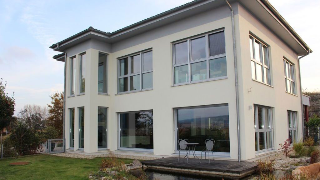 Moderne, weiße Stadtvilla in Holzbauweise mit großen Fensterfronten und Garten.